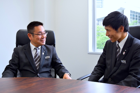 国際ハイヤー株式会社のベテランハイヤードライバー菅野さんと新卒ハイヤードライバー伊藤さんの話をしている写真