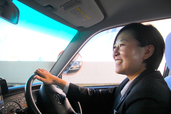 笑顔でタクシーを運転している国際自動車（㎞タクシー）株式会社に第二新卒で入社した女性タクシードライバー河原さんの写真