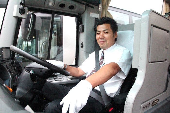 運転席で笑顔を向けるケイエム観光バス株式会社のバスドライバー阿部さんの写真