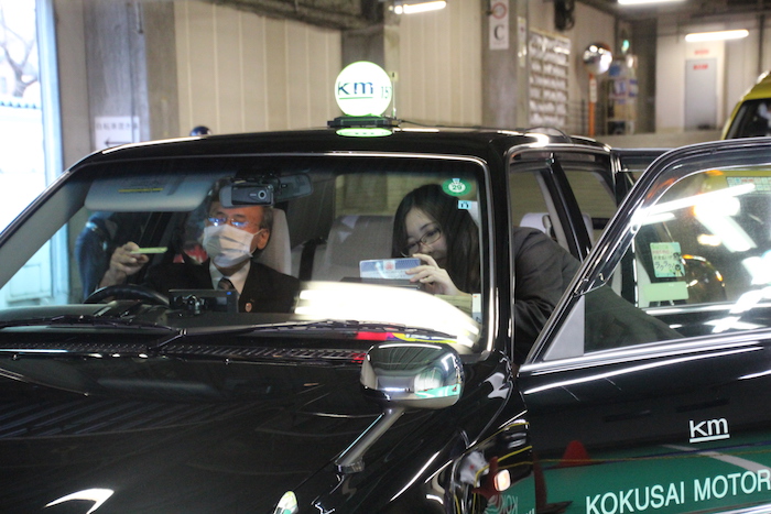 タクシーの助手席で作業している国際自動車（kmタクシー）株式会社板橋営業所職員の田島さんの写真