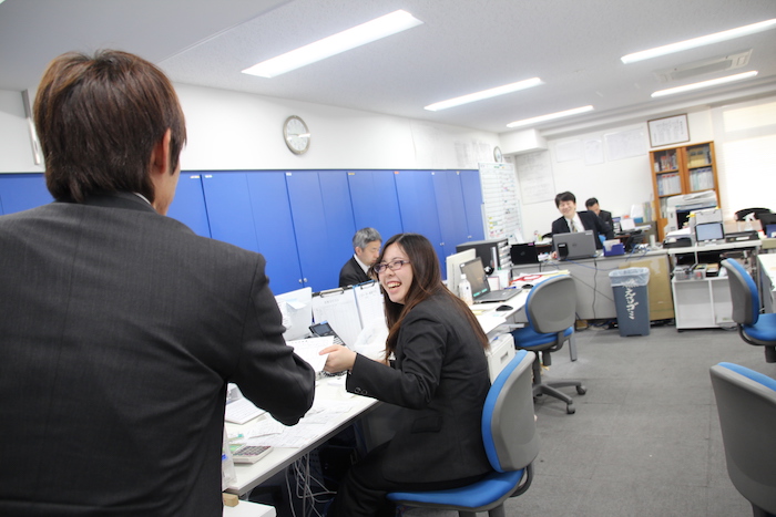 営業所のデスクで同僚と笑顔で話をしている田島さんの横顔の写真