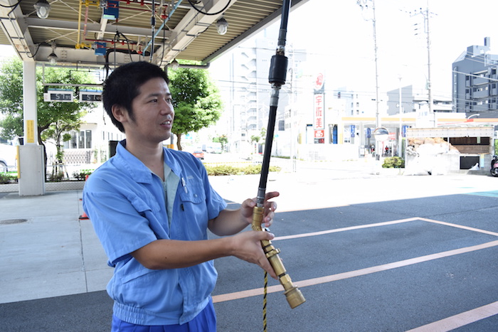 LPガススタンドで使用するノズルを持つ、国際自動車（㎞タクシー）のLPガススタンドで働く武原さんの写真